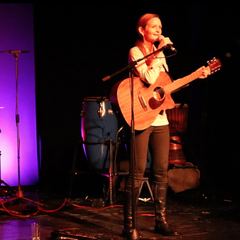 Kira Ludlow mit Gitarre auf einer Bühne in violettem Licht