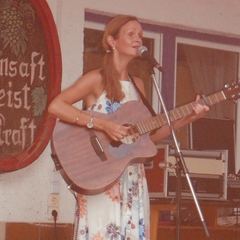 Kira Ludlow singt mit Gitarre vor einem bemalten Weinfass